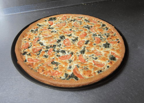 A freshly baked pizza topped with tomatoes and spinach on a golden crust, placed on a black pizza pan.