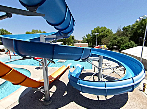 Aerial view of colorful water slides at a pool, with blue and orange slides curving over a clear water area.