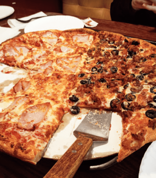 A large pizza with two sections: one topped with ham and cheese, the other with sausage and black olives.