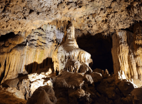 Stalactites and stalagmites in a dimly lit cave, showcasing intricate rock formations and textures.