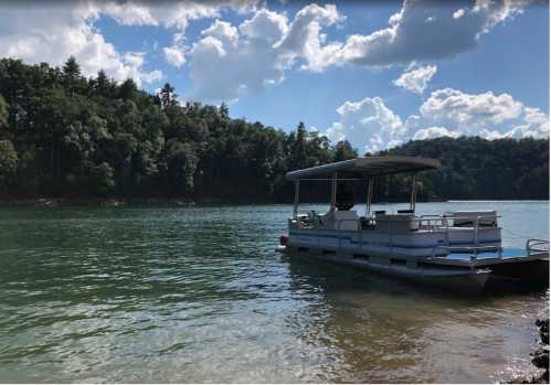 A boat anchored in calm waters near a forested shoreline under a partly cloudy sky.