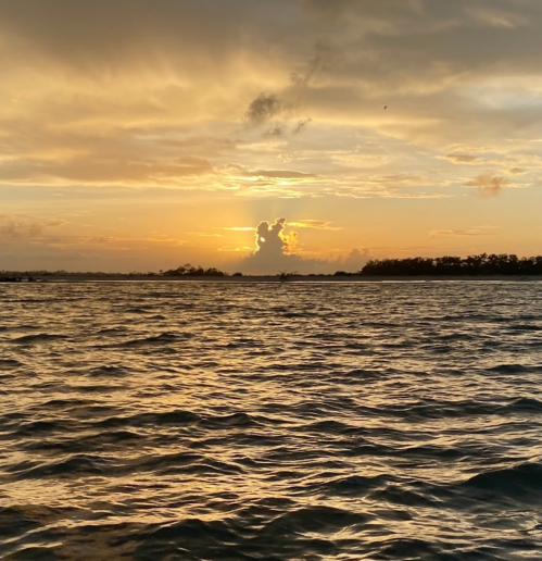 A serene sunset over a calm sea, with clouds reflecting warm hues in the sky.