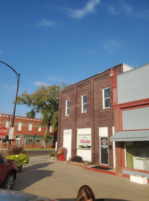 A brick building with a sign, surrounded by trees and a clear blue sky, in a small town setting.