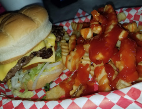 A cheeseburger with lettuce and tomato beside a serving of crinkle-cut fries topped with ketchup.