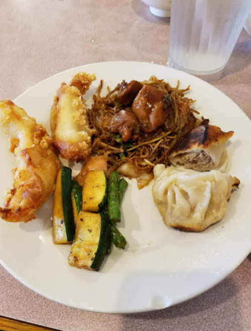 A plate of Chinese food featuring fried shrimp, noodles with chicken, dumplings, and sautéed zucchini and asparagus.