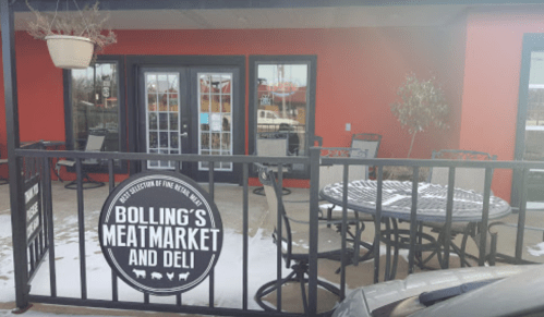 Exterior view of Bolling's Meat Market and Deli, featuring a patio with tables and a sign, set against a red wall.