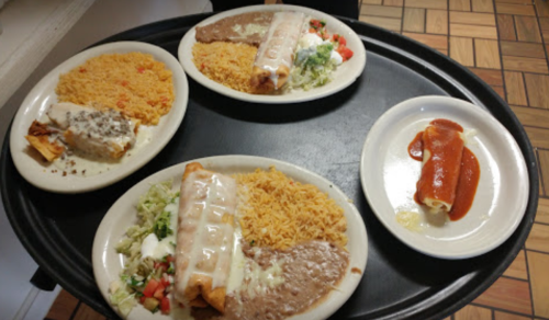 A tray with four plates of Mexican food, including enchiladas, rice, beans, and a side of sauce.