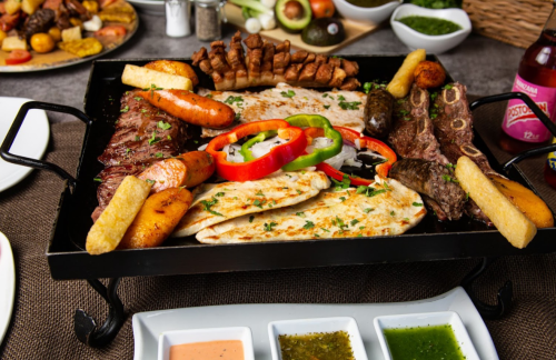 A vibrant platter of grilled meats, tortillas, and colorful peppers, served with sauces and sides.