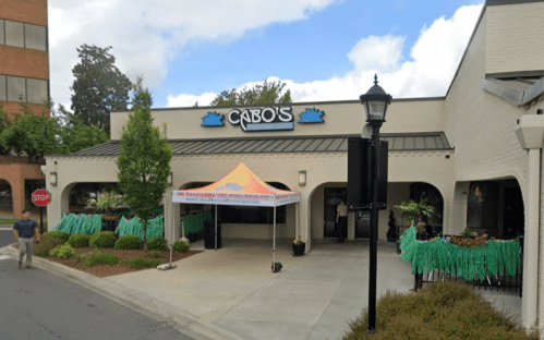 Exterior of Cabo's restaurant with a colorful tent, greenery, and a stop sign nearby on a sunny day.
