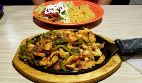 Sizzling chicken fajitas with bell peppers on a wooden platter, served with a side of rice and a fresh salad.