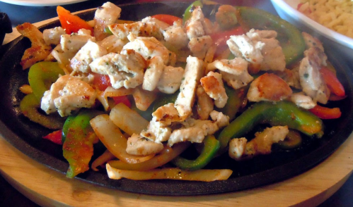 Sizzling fajitas with grilled chicken, bell peppers, and onions on a hot skillet.