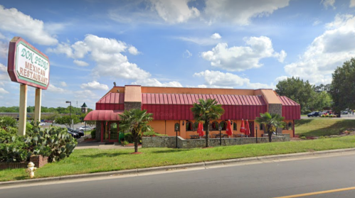 A colorful Mexican restaurant with a red roof, palm trees, and a sign, set against a blue sky with fluffy clouds.