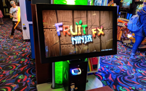 A colorful arcade game screen displaying "Fruit Ninja FX" with a vibrant carpet in the background.