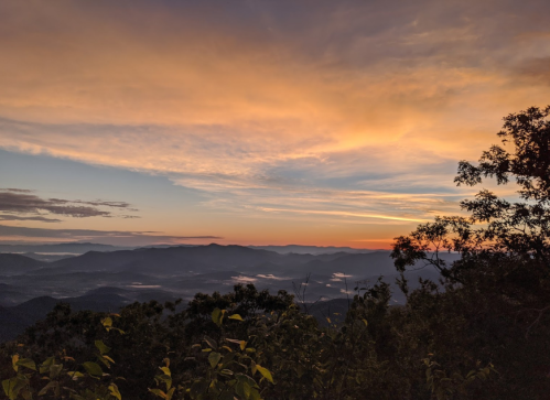 A scenic view of mountains under a colorful sunset, with clouds and mist in the valleys below.