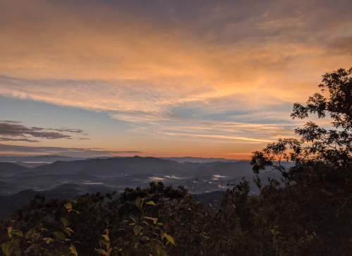 A scenic view of mountains under a colorful sunset, with clouds and mist in the valleys below.