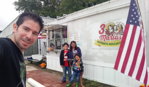 A man takes a selfie with a woman and two children outside a food truck named "3 Marias Authentic Mexican Food."
