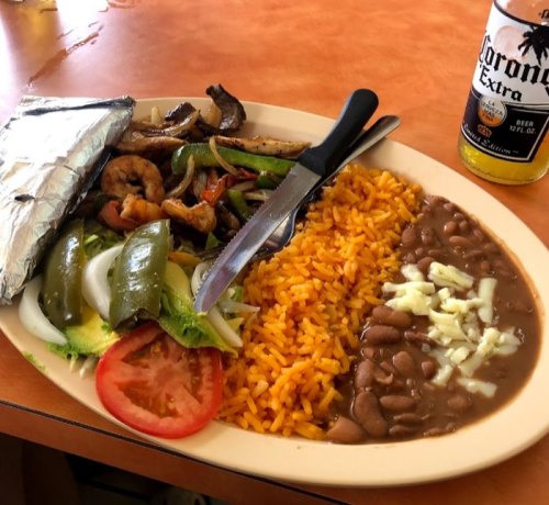A plate of colorful Mexican food with shrimp, grilled vegetables, rice, beans, and a beer on the side.