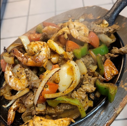 Sizzling platter of shrimp and beef with colorful bell peppers, onions, and tomatoes, steaming on a hot skillet.