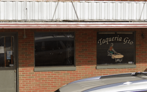 A brick building with a sign reading "Taqueria Gto" and an open window, featuring a person at a table.