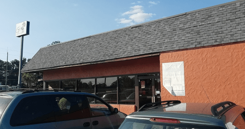 Exterior of a restaurant with an orange wall and a gray roof, parked cars in front, under a clear blue sky.