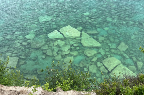 Clear turquoise water reveals submerged rocks and greenery along the shoreline.