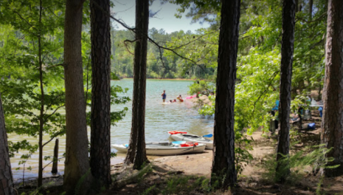 A serene lake scene framed by trees, with people enjoying the water and kayaks on the shore.