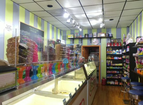 A colorful ice cream shop interior with a display of ice cream tubs, candy shelves, and striped walls.