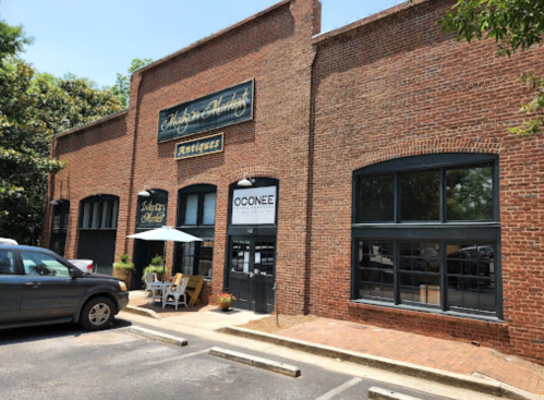 A brick building with large windows, featuring a sign for "Oconee" and outdoor seating in front.