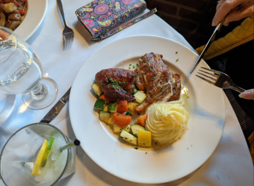 A plate with roasted chicken, mashed potatoes, and mixed vegetables, accompanied by a glass of water and a colorful wallet.