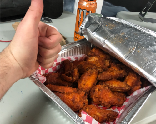 A hand giving a thumbs up next to a tray of crispy chicken wings and a can of Monster energy drink.