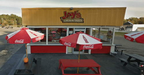 Exterior of Jay's Chicken Shack with red picnic tables and Coca-Cola umbrellas, featuring an open sign.