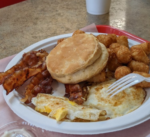 A plate of breakfast featuring a biscuit, bacon, tater tots, and a fried egg.