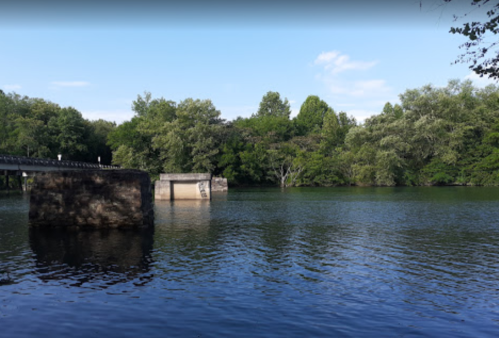 A serene river scene with lush green trees and a stone bridge reflecting in the calm water under a clear blue sky.