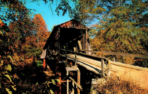 A rustic covered bridge surrounded by vibrant autumn foliage and clear blue skies.