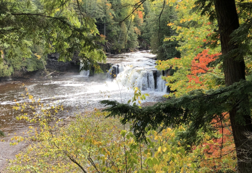 A serene waterfall surrounded by vibrant autumn foliage and lush green trees.