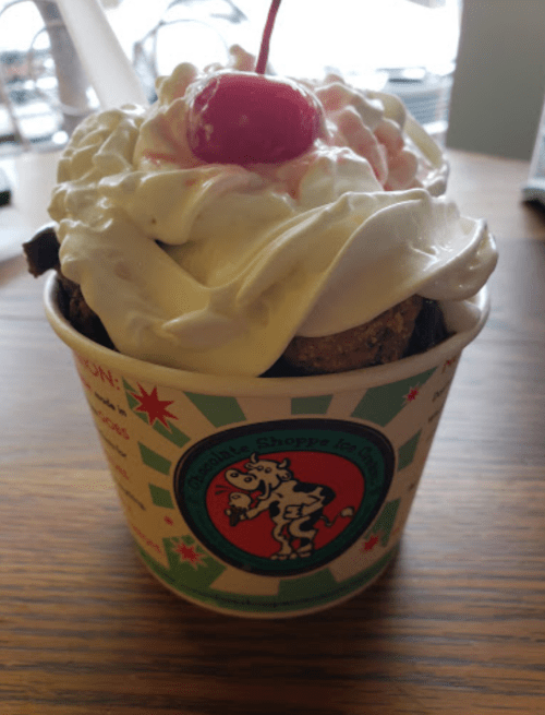 A cup of ice cream topped with whipped cream and a cherry, featuring a festive design.