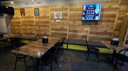Interior of a casual dining space with wooden walls, tables, and chairs, featuring a TV and framed artwork.