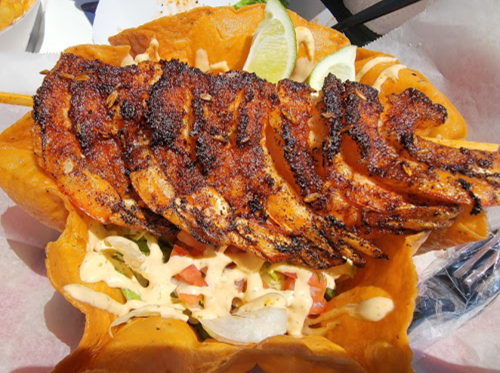 Grilled shrimp skewers on a bed of lettuce and tomatoes, served in a crispy tortilla bowl with sauce and lime wedges.
