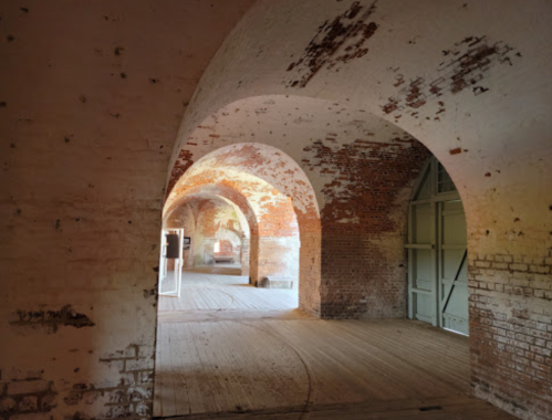 Interior of a historic brick building with arched doorways and wooden flooring, showcasing weathered walls and soft lighting.