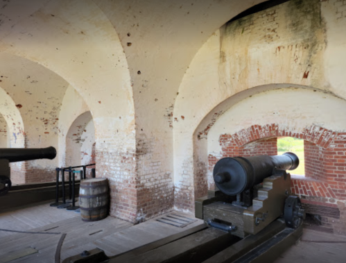 Interior of a historic fort with arched brick walls and cannons positioned near windows.