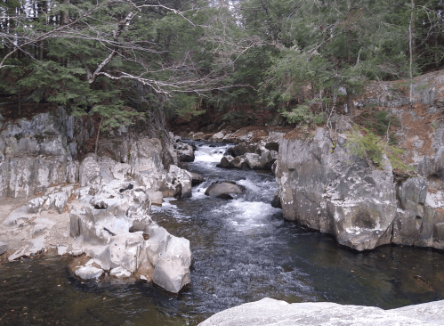 A serene river flows through rocky terrain, surrounded by lush green trees and a peaceful natural landscape.