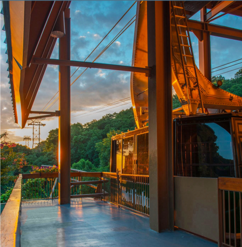 A scenic view from a balcony at sunset, featuring modern architecture and lush greenery in the background.