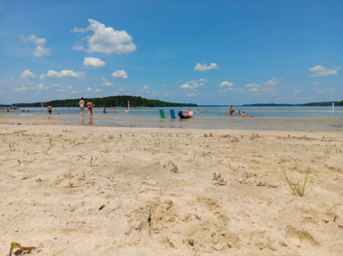 A sandy beach with people enjoying the water and sun under a blue sky with fluffy clouds.