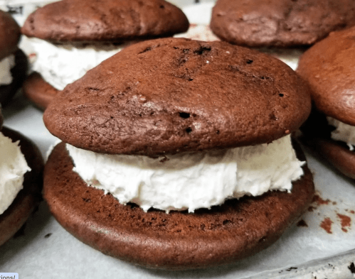 Close-up of chocolate whoopie pies filled with white cream, resting on a baking sheet.