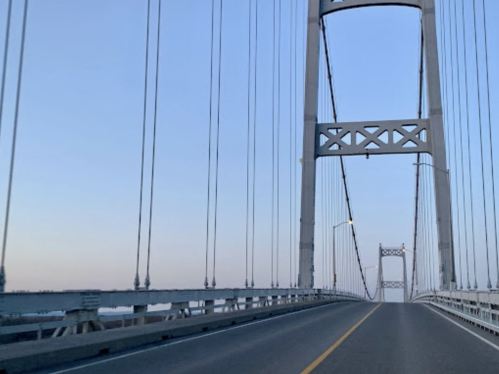 A view of a suspension bridge at dusk, with a clear sky and a road leading towards the bridge's center.