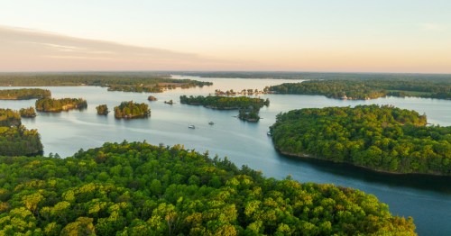 Aerial view of a serene lake surrounded by lush green islands and trees under a clear sky.