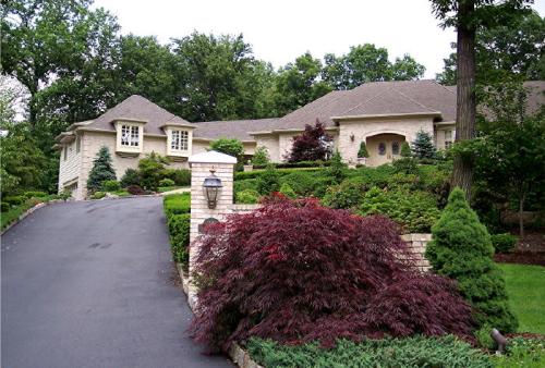 A landscaped home with a stone exterior, surrounded by trees and shrubs, on a winding driveway.