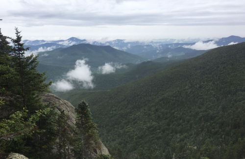 A panoramic view of lush green mountains and valleys under a cloudy sky, with mist hovering over the landscape.