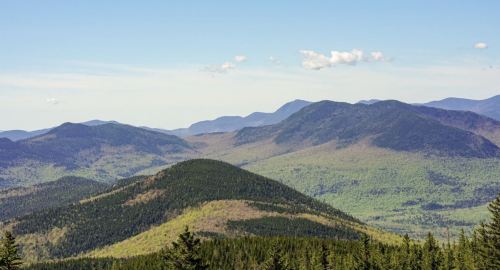 A panoramic view of rolling green mountains under a clear blue sky with a few clouds.