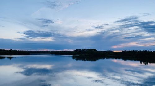 A serene lake at dusk, reflecting a blue sky with scattered clouds and hints of sunset colors on the horizon.